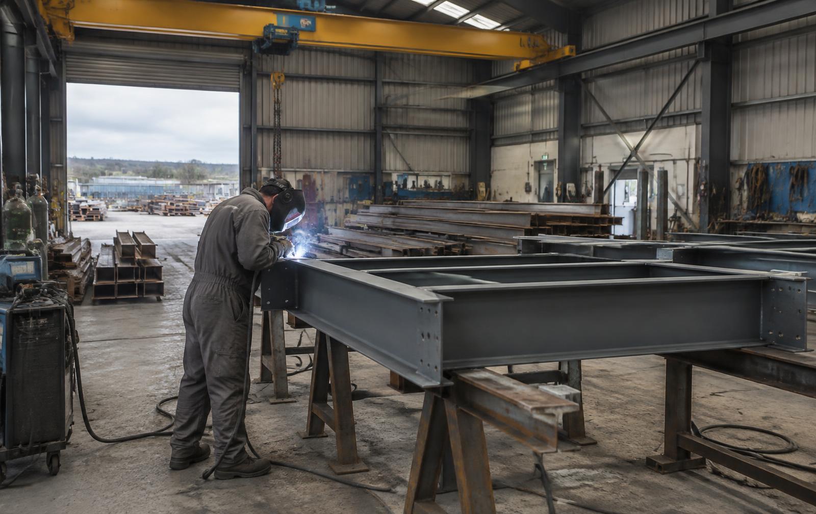 Welder fabricating a structural steel frame in a workshop (illustrative)